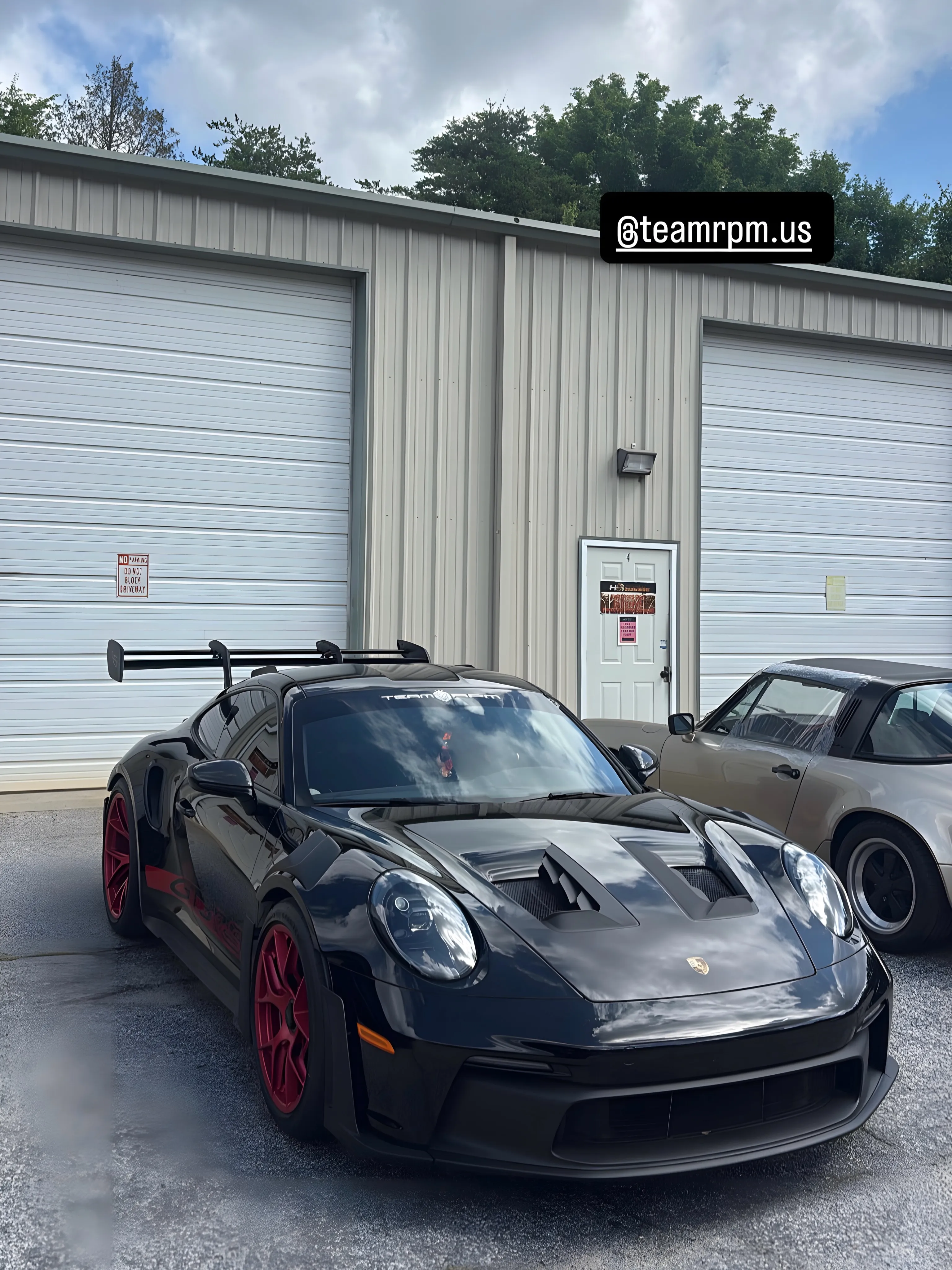 Black Porsche 911 GT3 RS on red wheels at the shop