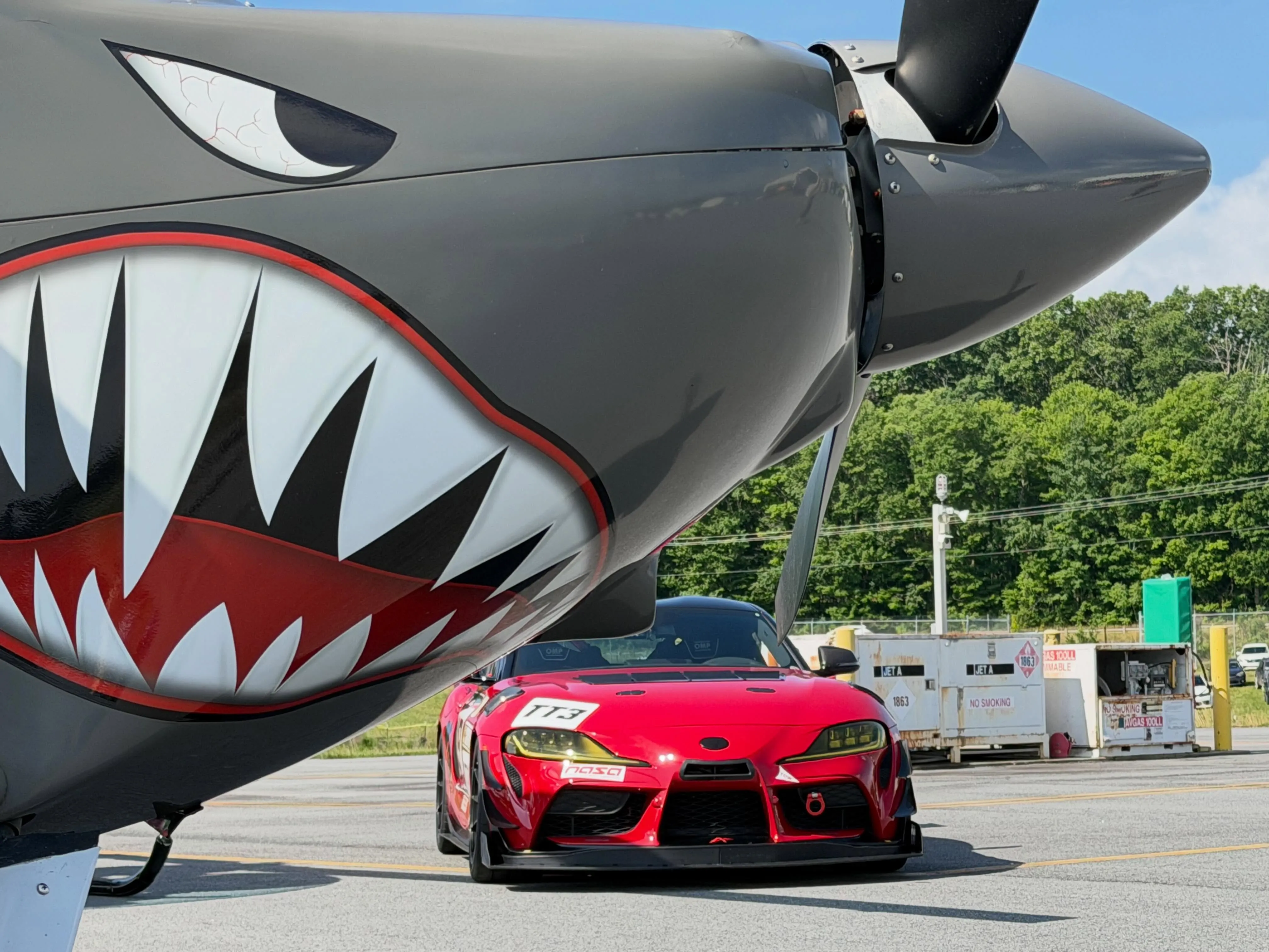 Red GR Supra race car under a shark-mouth warbird airplane nose